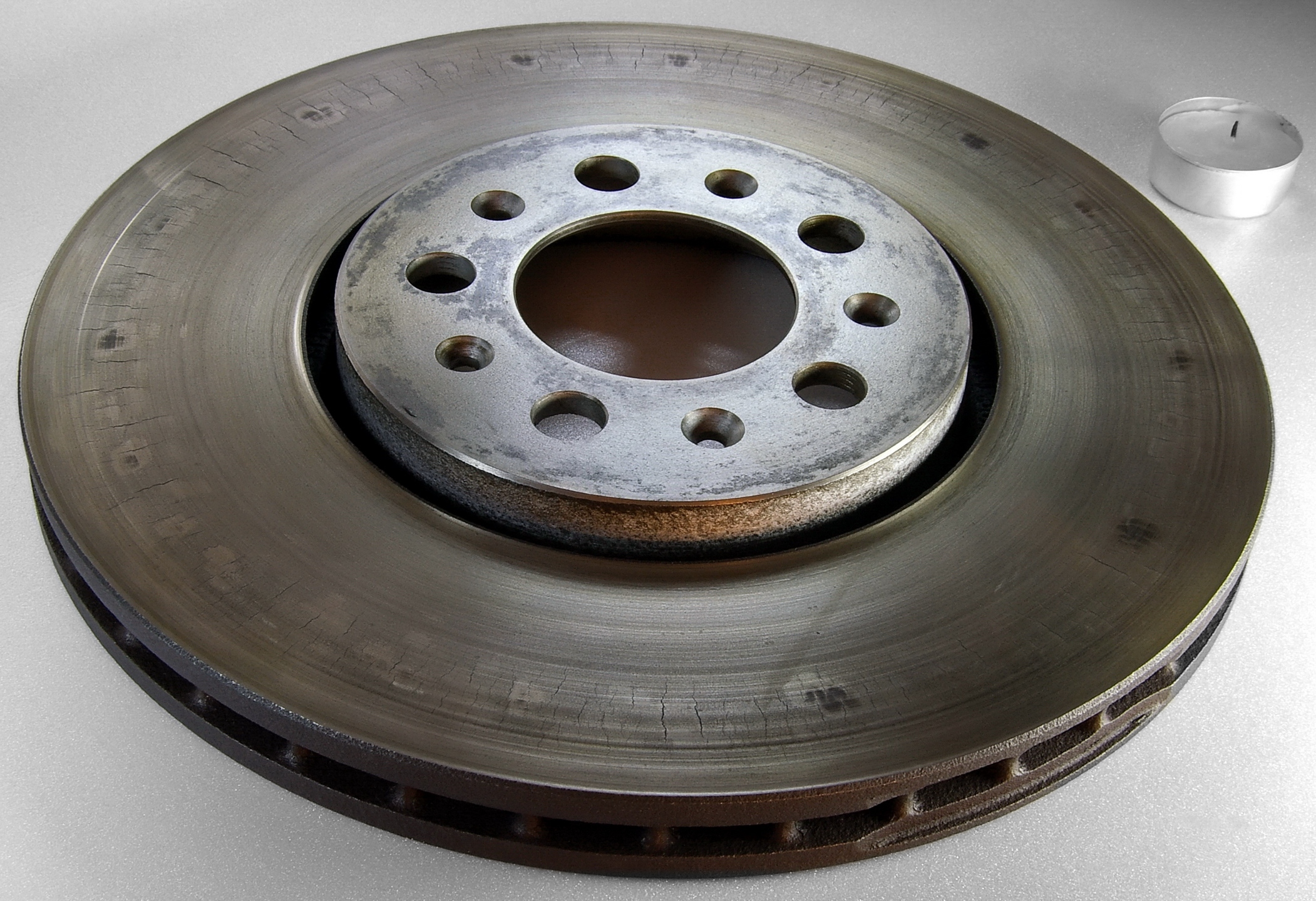 Worn ventilated passenger-car brake rotor with heat-related cracks, tea light for scale